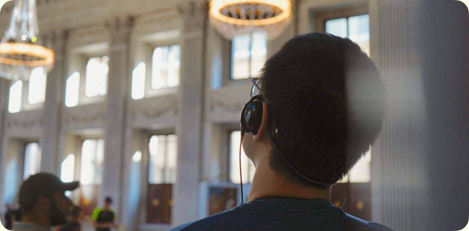 A visitor wearing headphones inside a hall with chandeliers