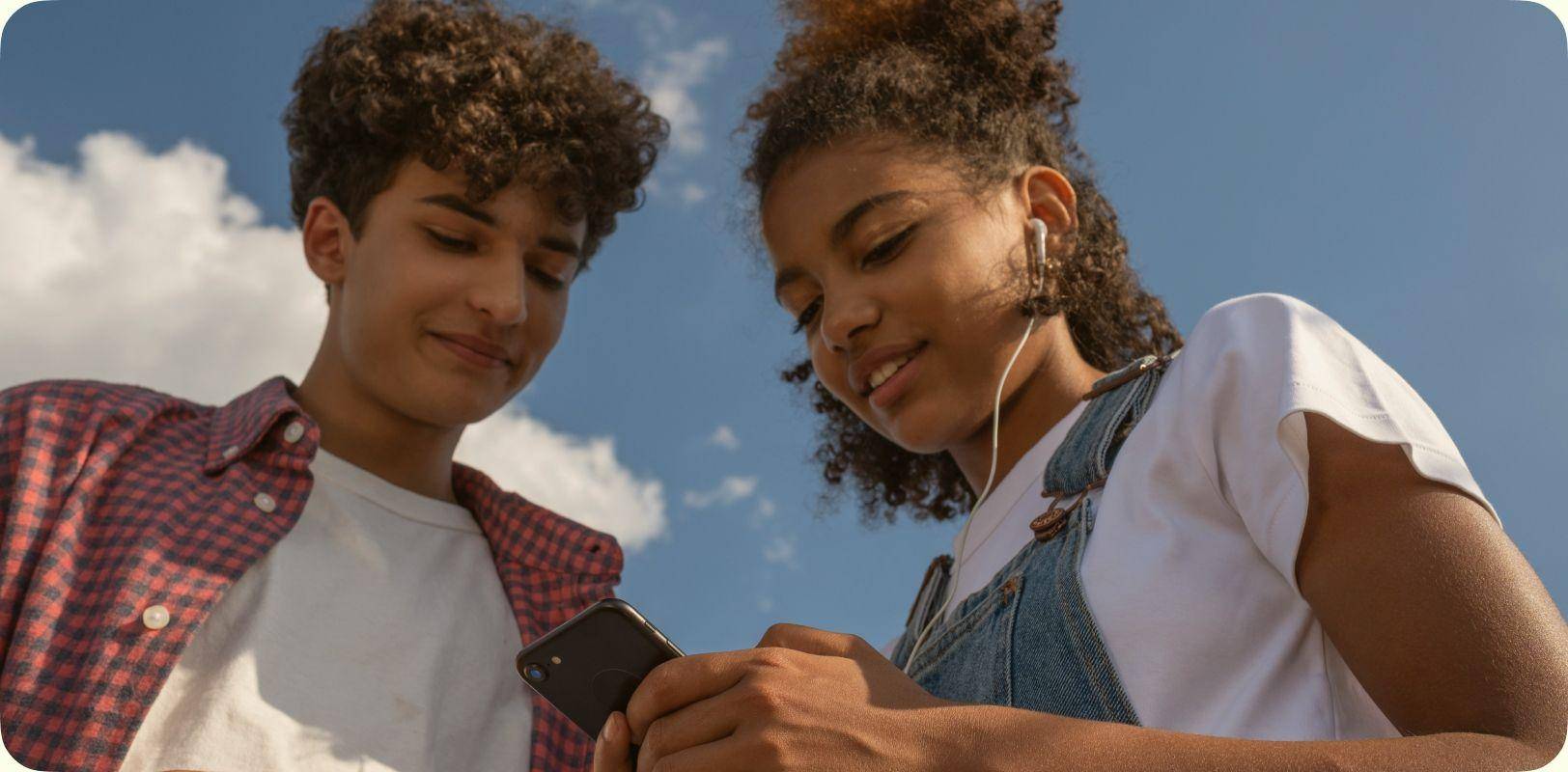Two teenagers look together at a smartphone outdoors