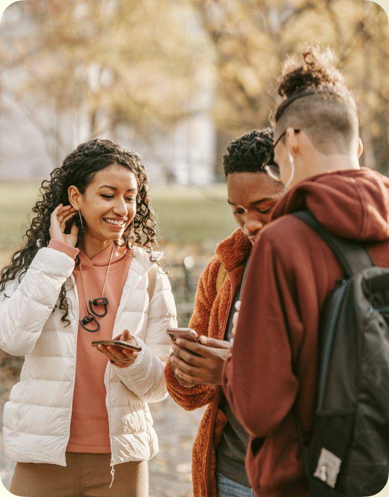 Three young travellers look at their phones in a city park